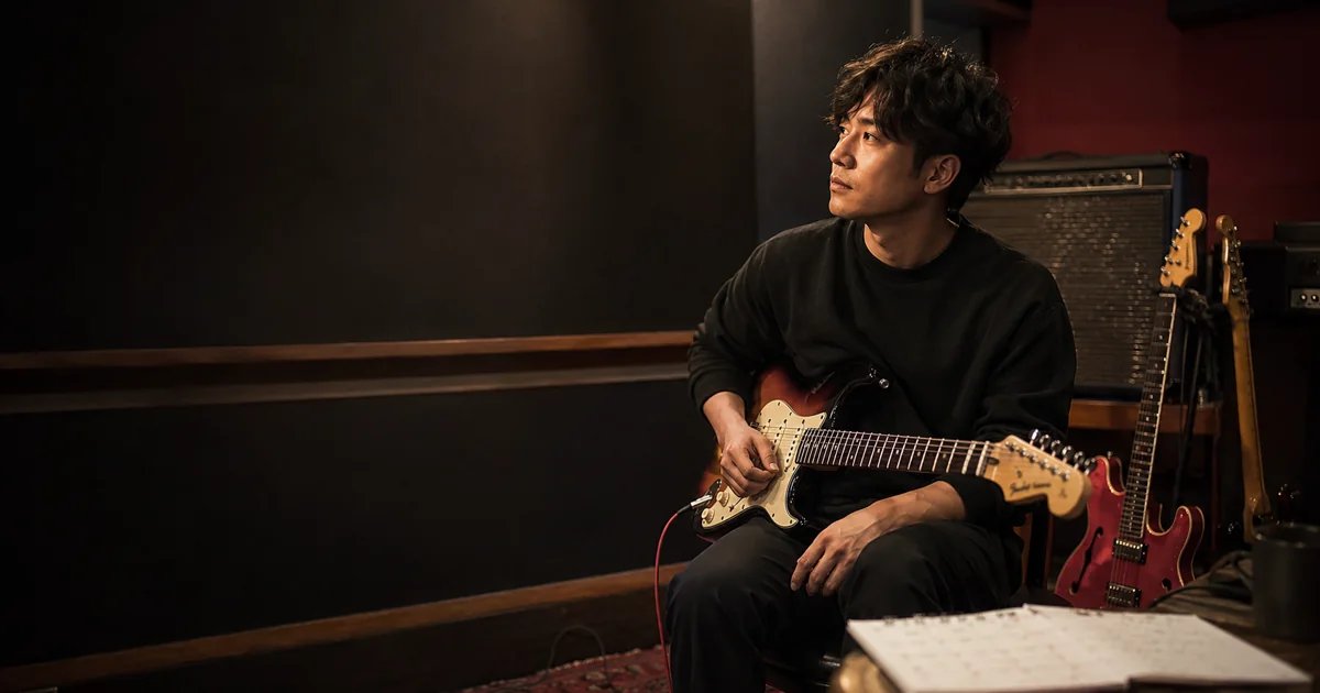 落ち着いた音楽スタジオでギターを構え、自分のペースで次の音を考える男性